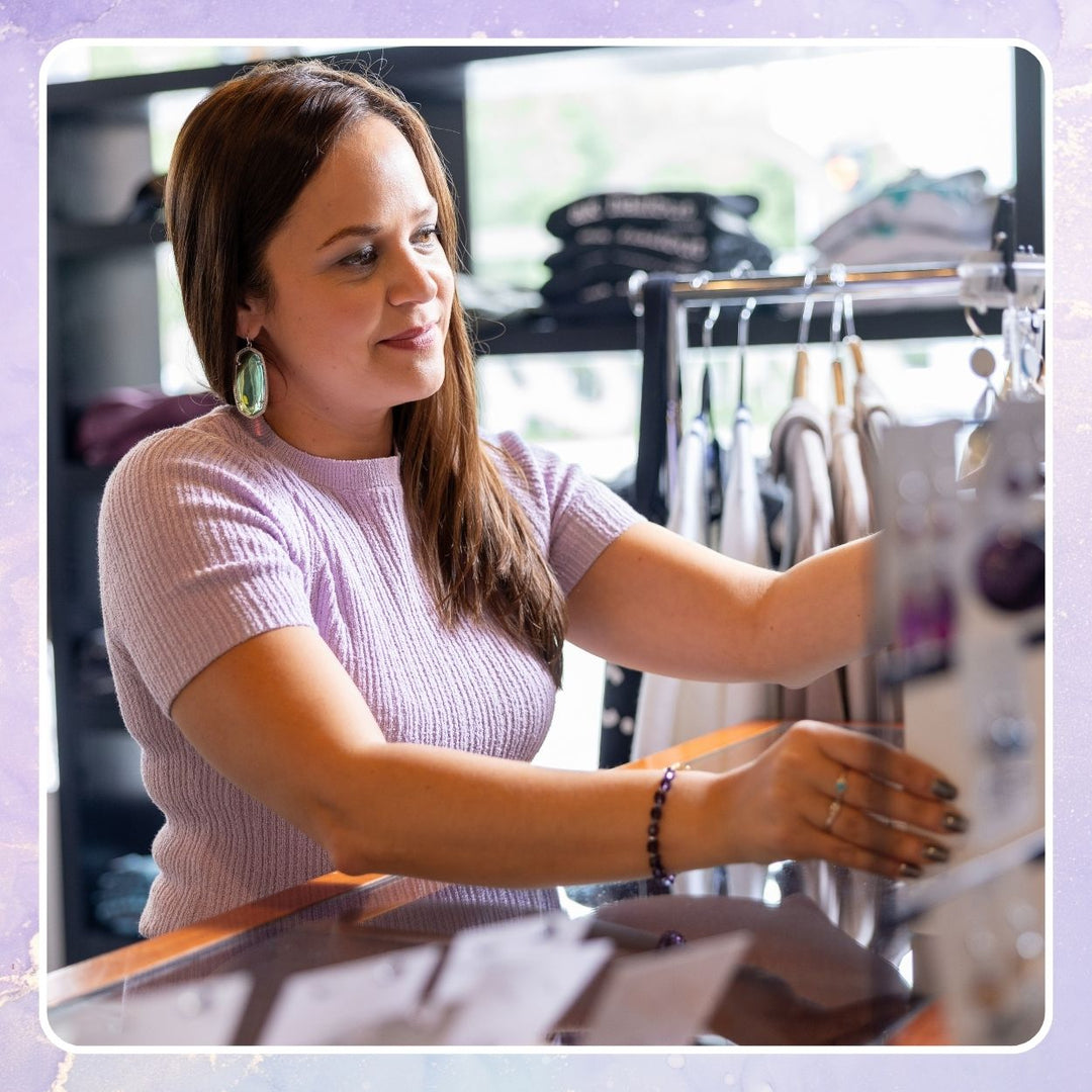 Woman using a tablet point-of-sale system at a boutique checkout counter with clothing racks behind her.