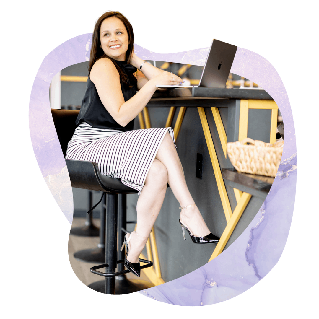 Woman seated at a table using a laptop in a modern workspace with a lavender abstract frame.